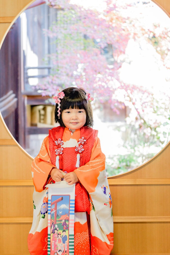 芦屋神社のご本殿の丸窓の前に立つ、晴れ着のお子さま